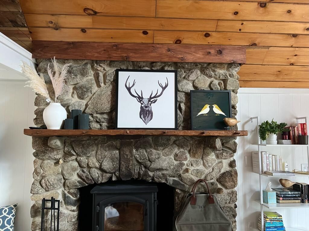 A stone fireplace with a wooden mantel shelf displaying framed artwork and decorative items.