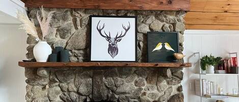 A stone fireplace with a wooden mantel shelf displaying framed artwork and decorative items.