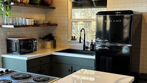 Una cocina moderna con una isla central, estufa integrada, refrigerador negro y utensilios colgantes.