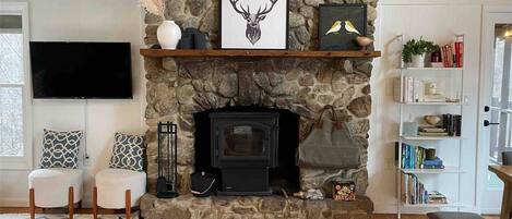A cozy living room with a stone fireplace, a flat-screen TV, two patterned chairs, and a bookshelf.