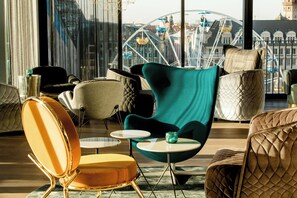 En moderne lounge med behagelige siddepladser, udsigt til et pariserhjul og et bybillede.