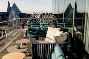 En tagterrasse med siddepladser, et pariserhjul og en markant bygning med spidse tårne i baggrunden.