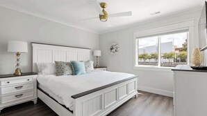 Een slaapkamer met een bed, nachtkastjes, een dressoir, een plafondventilator, een raam met uitzicht en een wanddecoratie.