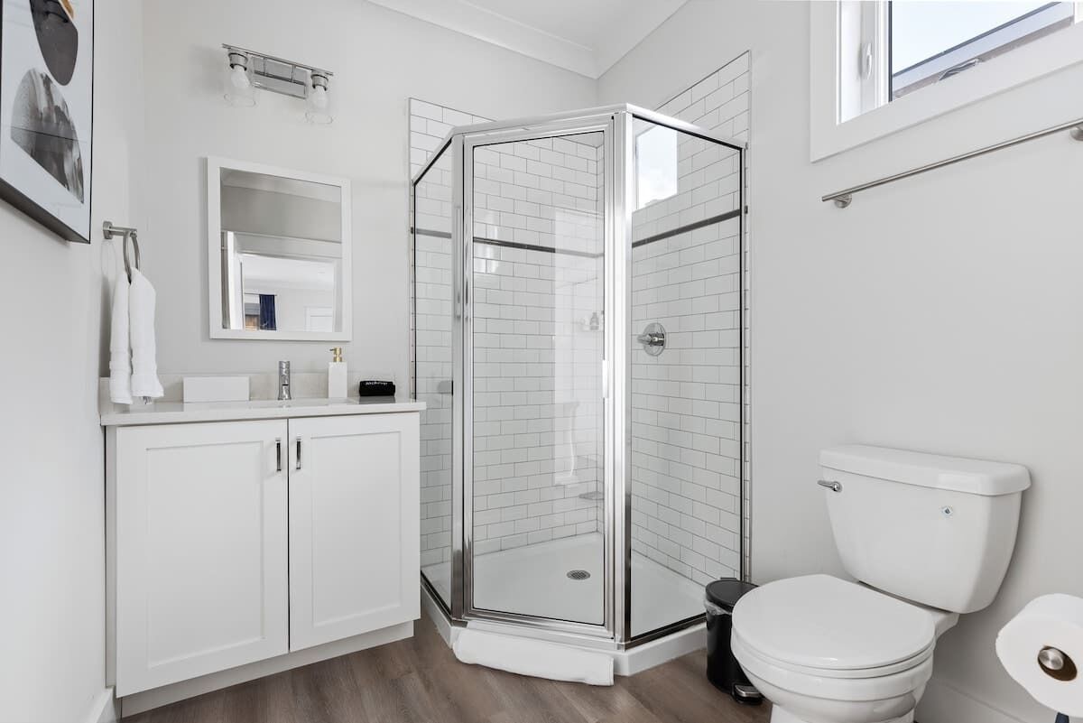 Un baño moderno con cabina de ducha de vidrio, inodoro blanco y lavabo con espejo sobre él.