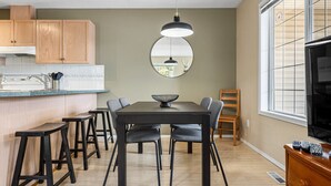 A modern kitchen with a dining area, wooden cabinets, a large window, and a television.