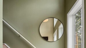 A staircase with wooden steps and white handrails, a round mirror on the wall, and a window with a view of trees.