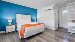 A hotel room with a bed, nightstands, a wardrobe, and an air conditioning unit.
