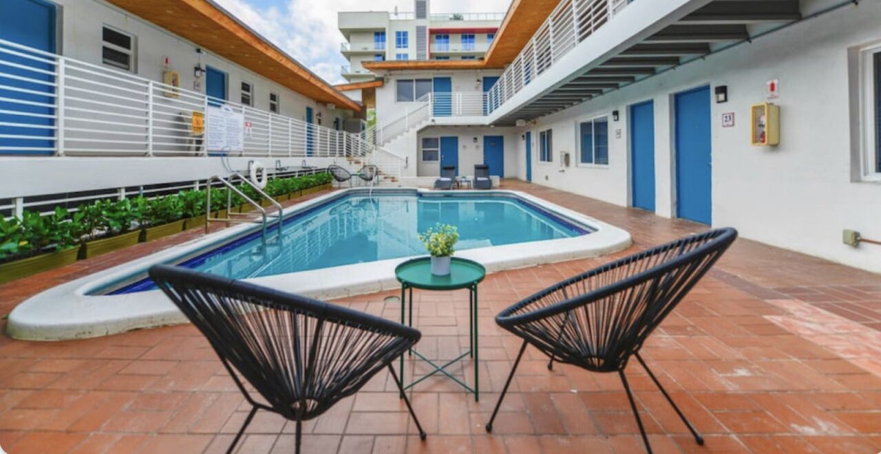 A swimming pool with two chairs and a table, surrounded by a building with multiple floors and balconies.