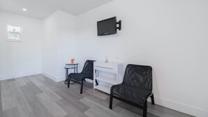 Una habitación con dos sillones de cuero negro, una mesita blanca con un florero, un armario blanco y un televisor montado en la pared.