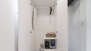 A small, white, enclosed bathroom with a shower, a shelf with towels, and a small storage unit.