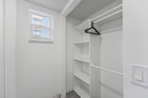 A white closet with shelves and a hanging rod, a small window, and a light switch on the wall.