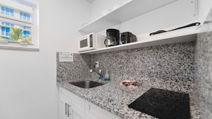 A kitchen with granite countertops, a stainless steel sink, a coffee maker, and a toaster on a white shelf.