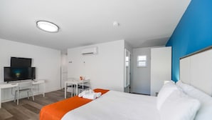 A hotel room with a bed, a desk, a television, and an air conditioning unit.