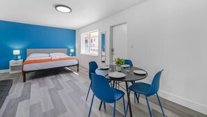 Una habitación moderna con una cama, una mesa de comedor con sillas y un ventanal pequeño.