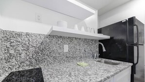 Una cocina con encimeras de granito, un refrigerador de acero inoxidable y un estante blanco sobre el fregadero.