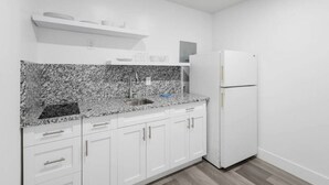 A kitchen with white cabinets, a granite countertop, a sink, and a white refrigerator.