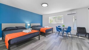 Una habitación de hotel con dos camas, un escritorio y sillas, y un ventanal.