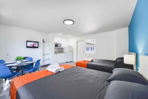 Une chambre d’hôtel avec deux lits, un bureau avec une chaise, une télévision et une kitchenette.