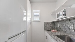 Una cocina compacta con armarios blancos, encimera de granito, pileta de acero inoxidable y un microondas.