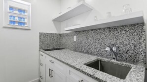 Una cocina con encimeras de granito, armarios blancos, un lavamanos doble y una ventana con persianas azules.