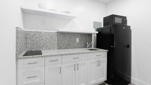 Una cocina con armarios blancos, encimera de granito, refrigerador negro y microondas.