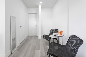 Un couloir avec une porte, une petite table sur laquelle est posé un vase, et deux chaises.