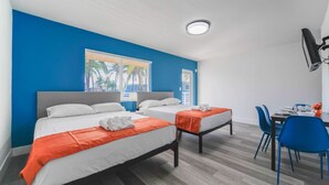 A hotel room with two beds, a desk with chairs, and a window with blinds.