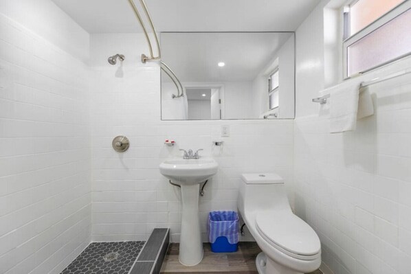 Un baño pequeño con paredes blancas, un lavamanos pedestal, un inodoro y una zona de ducha.