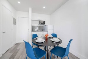 A modern dining area with a round table, blue chairs, and a kitchen in the background.