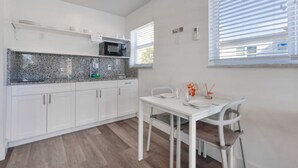 Una cocina moderna con armarios blancos, encimera de granito y comedor con mesa y sillas blancas.