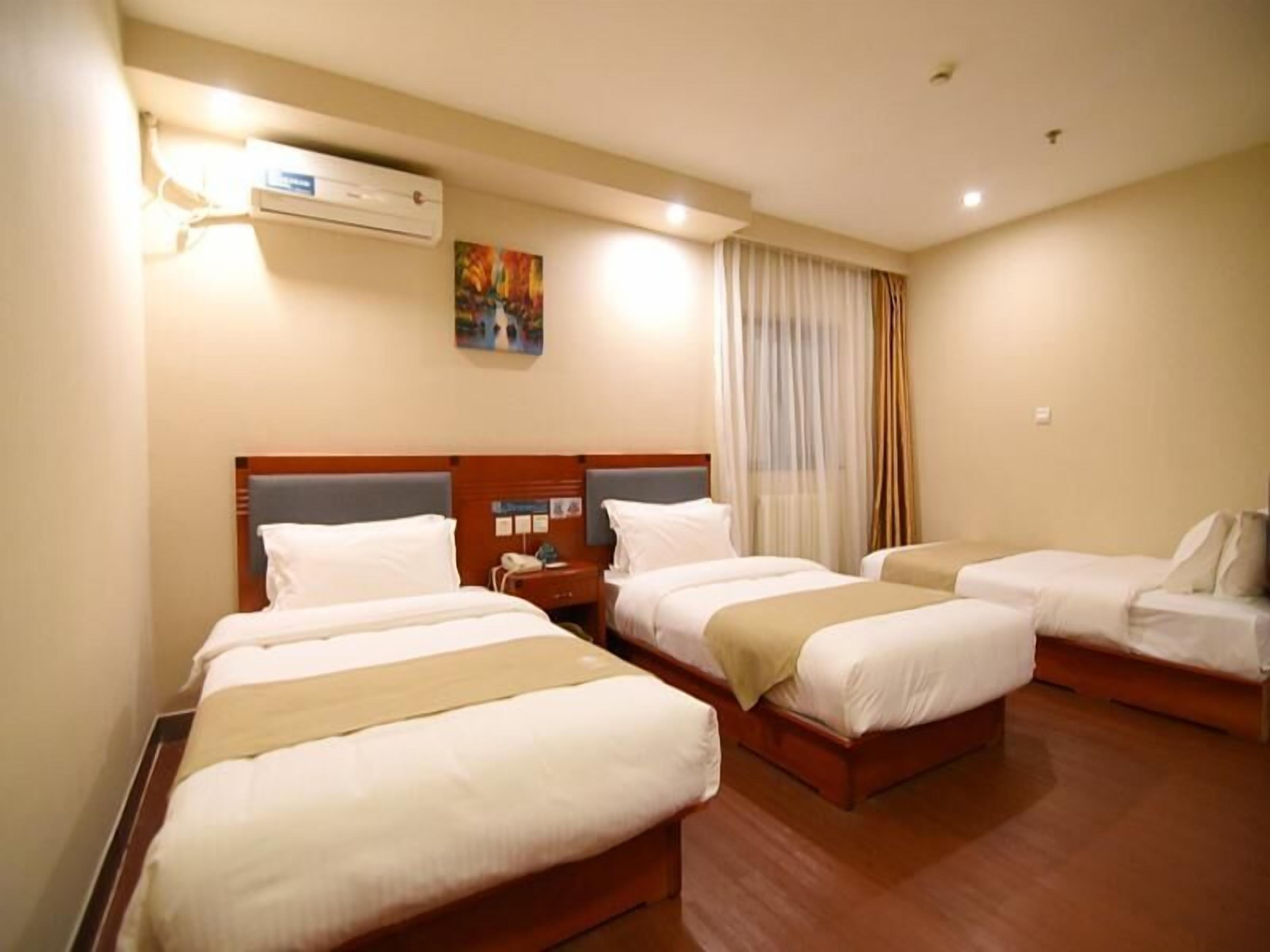A hotel room with three single beds, a wooden headboard, a bedside table with a phone, and an air conditioning unit on the wall.