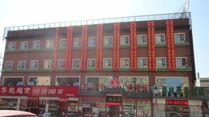 A multi-story building with a red facade and multiple windows. There are storefronts with signage, a visible phone number, and a parking lot with vehicles. - Greentree Inn Beijing Chaoyang District Happy Valley Express Hotel (Beijing)