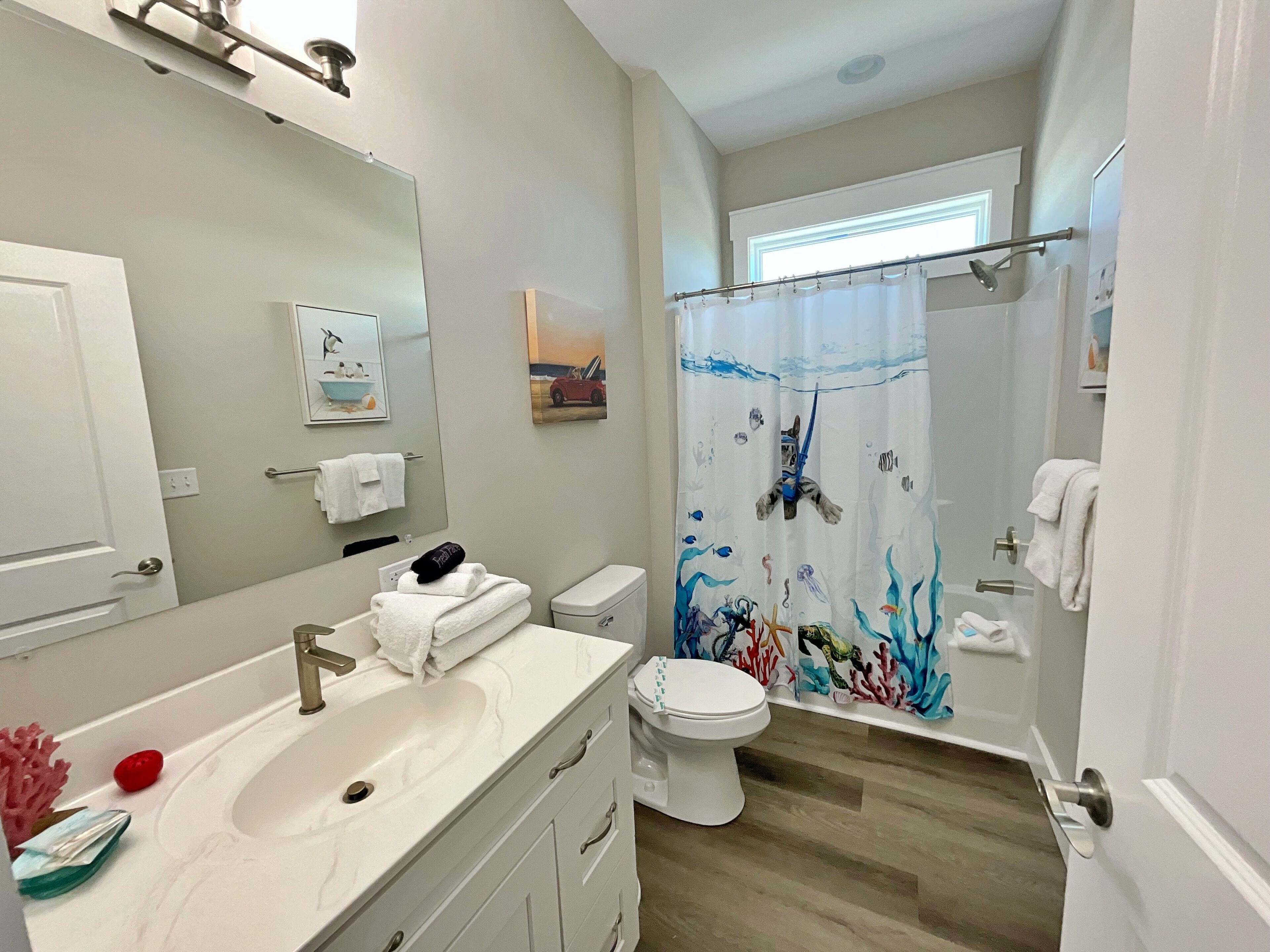 Un baño con un lavabo blanco, un inodoro y una ducha con cortina de baño de temática submarina y colores vivos.