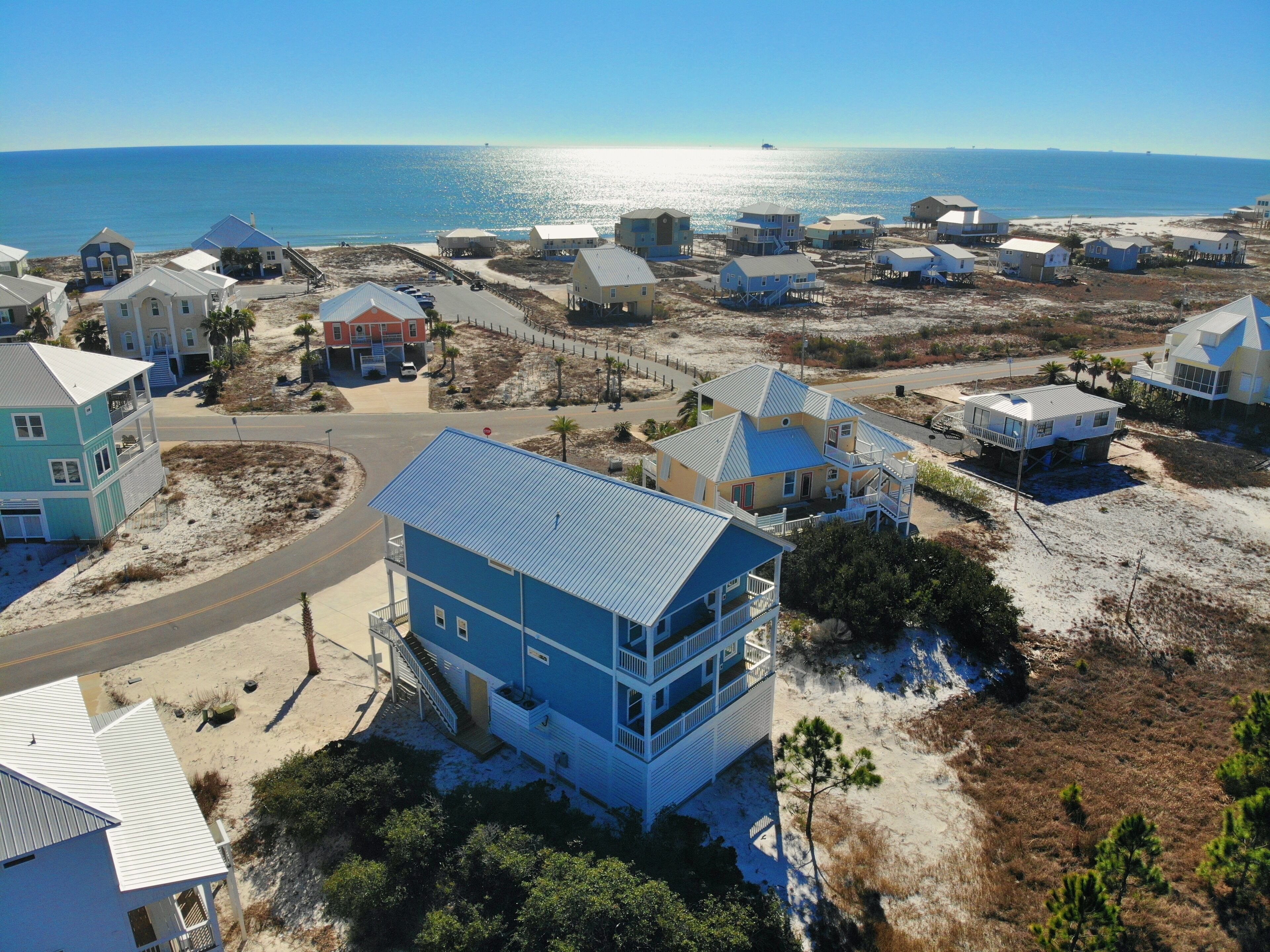 A coastal residential area with houses, some elevated on stilts, and a road leading to the beach.