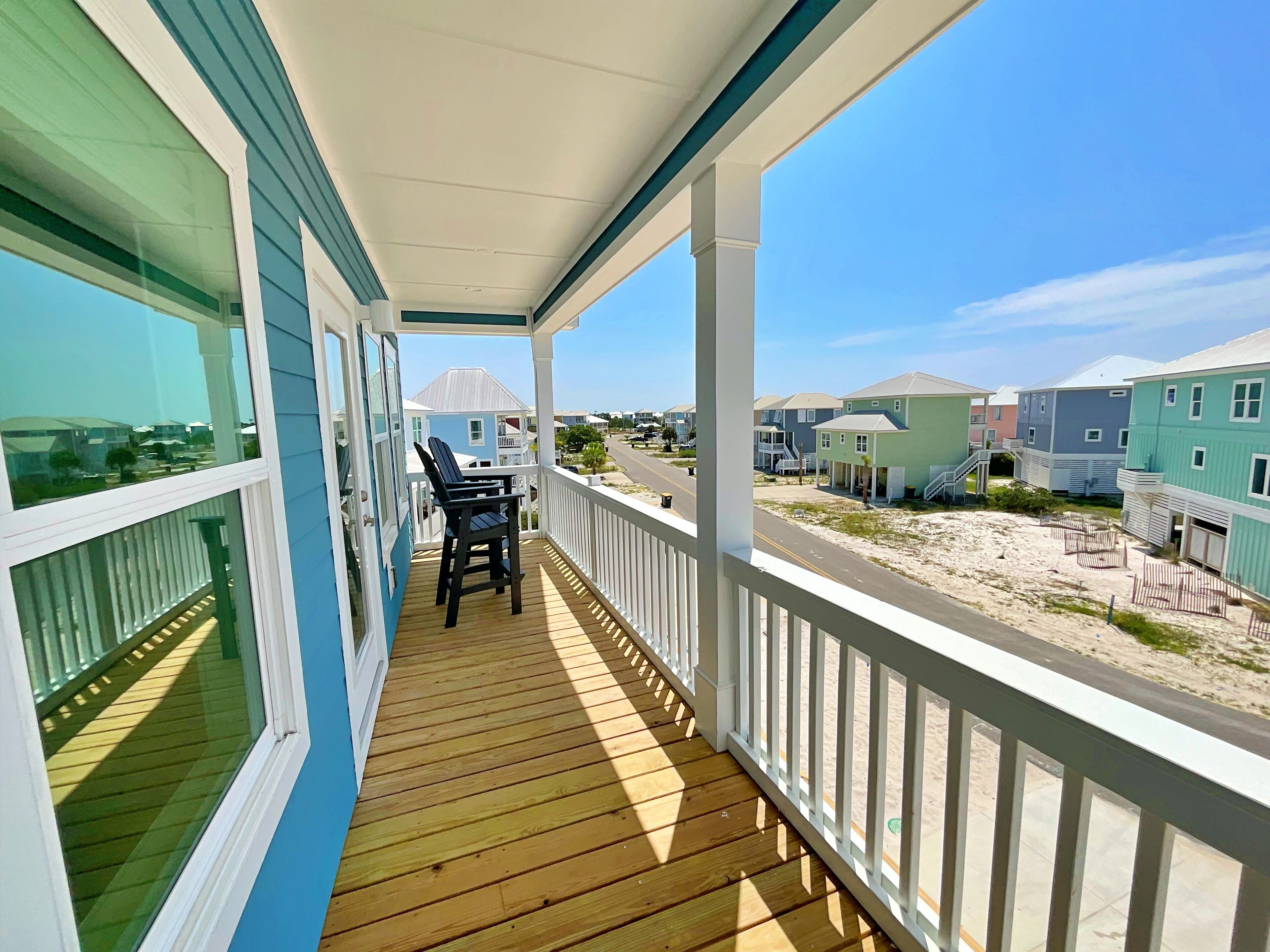 Um deck de madeira com mesa e cadeiras, com vista para uma praia e casas coloridas.