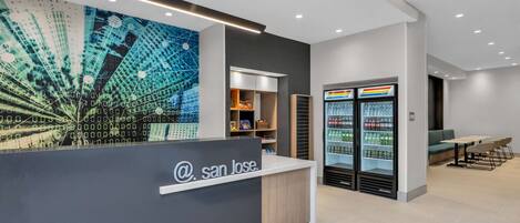 A modern reception area with a digital mural, a reception desk, a seating area, and a refrigerator stocked with beverages.