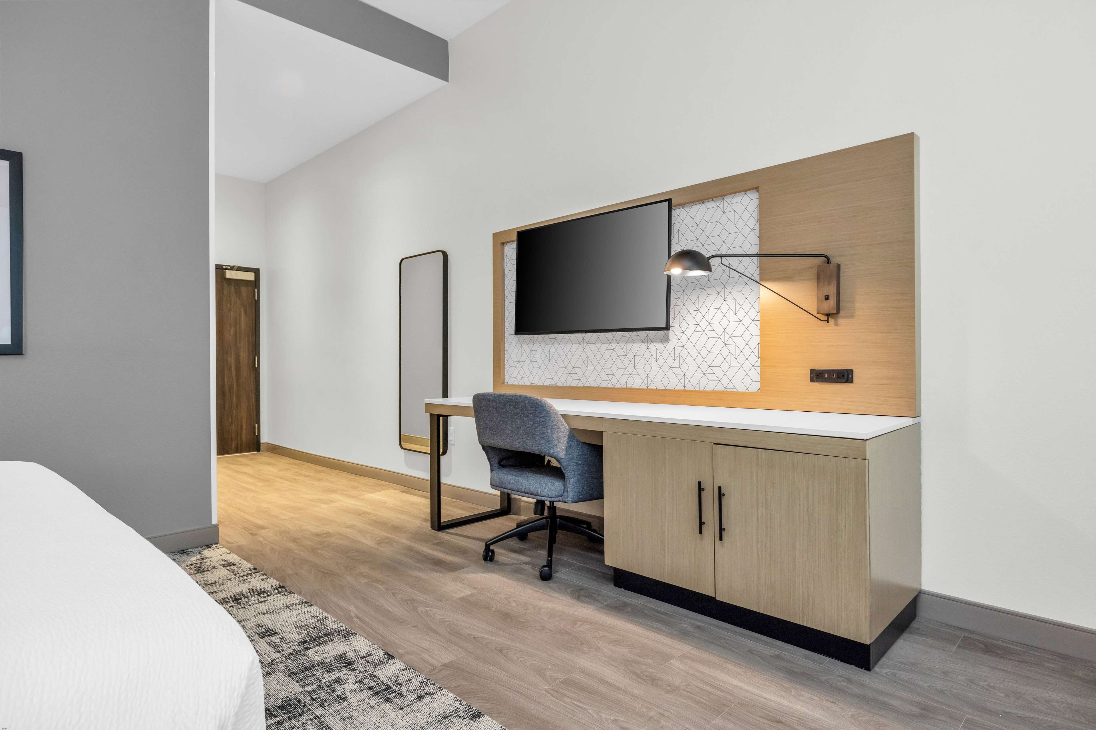 Een moderne slaapkamer met een groot bed, een bureau met stoel, en een tv aan de muur.