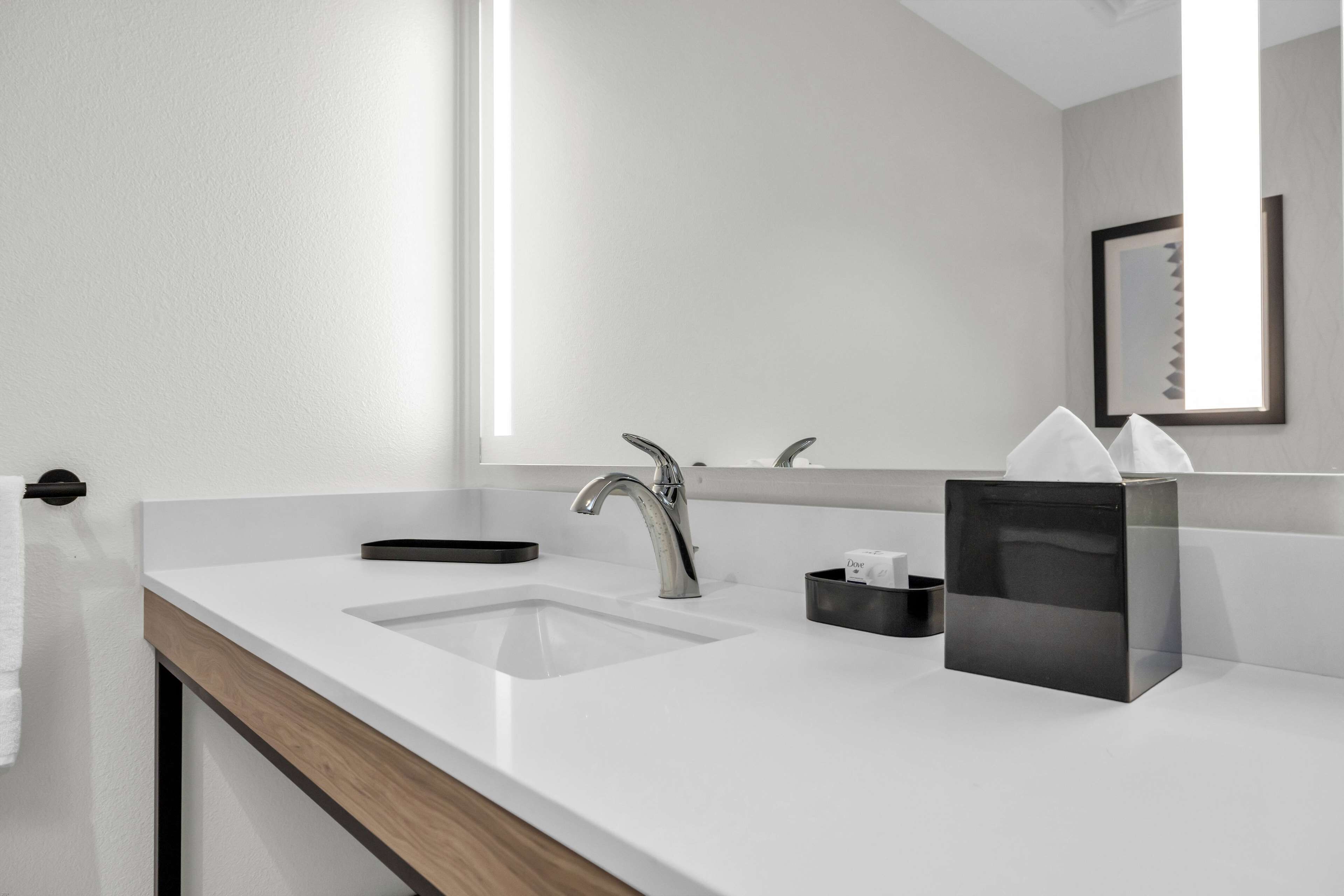 A modern bathroom with a white sink, a mirror, and a black tissue box.