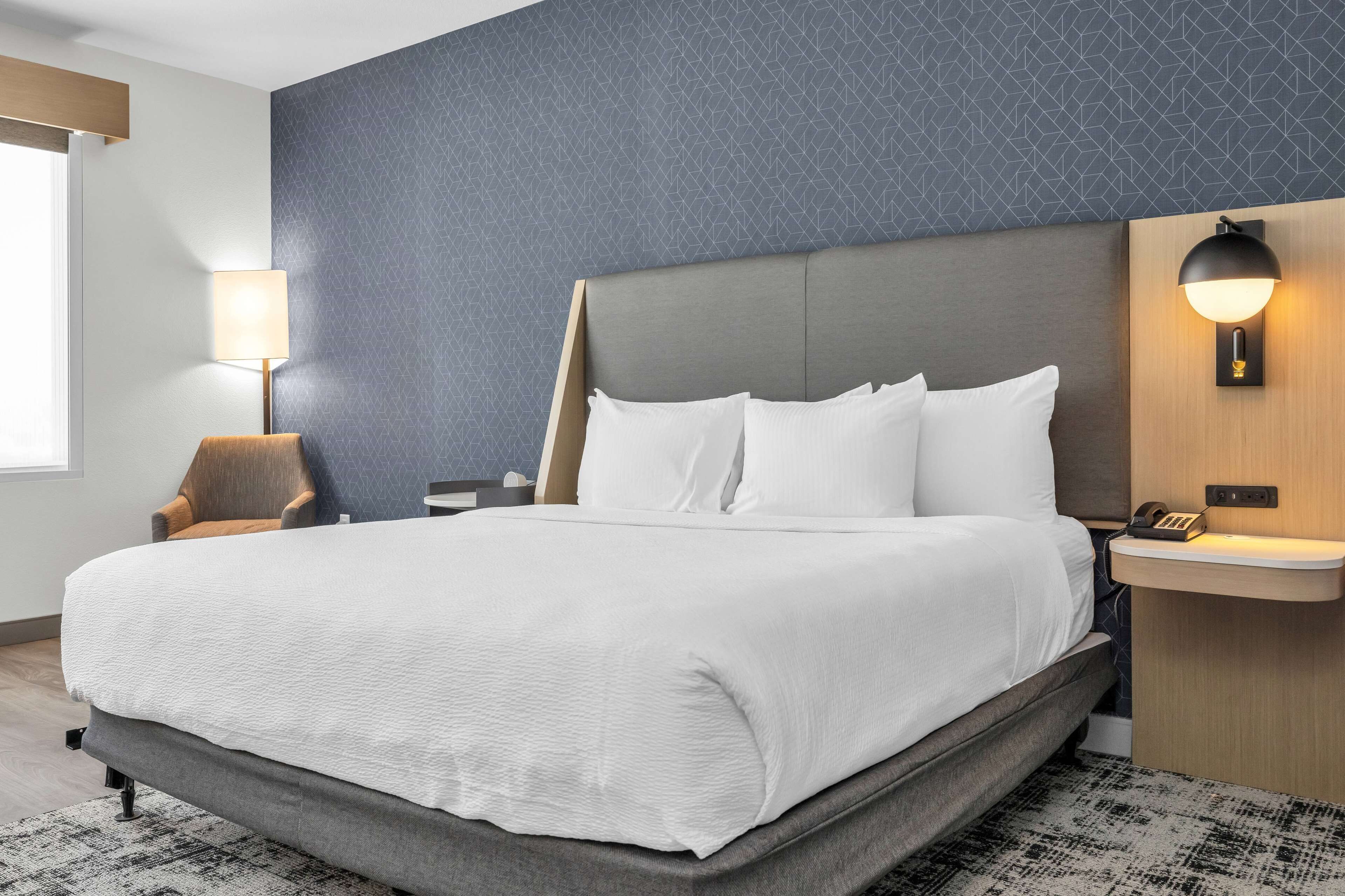 A modern hotel room with a large bed, a nightstand, a lamp, and a wall-mounted phone.