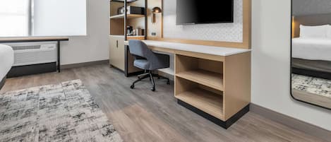 Habitación de hotel moderna con una cama grande, un escritorio con televisor, una silla y estanterías empotradas.