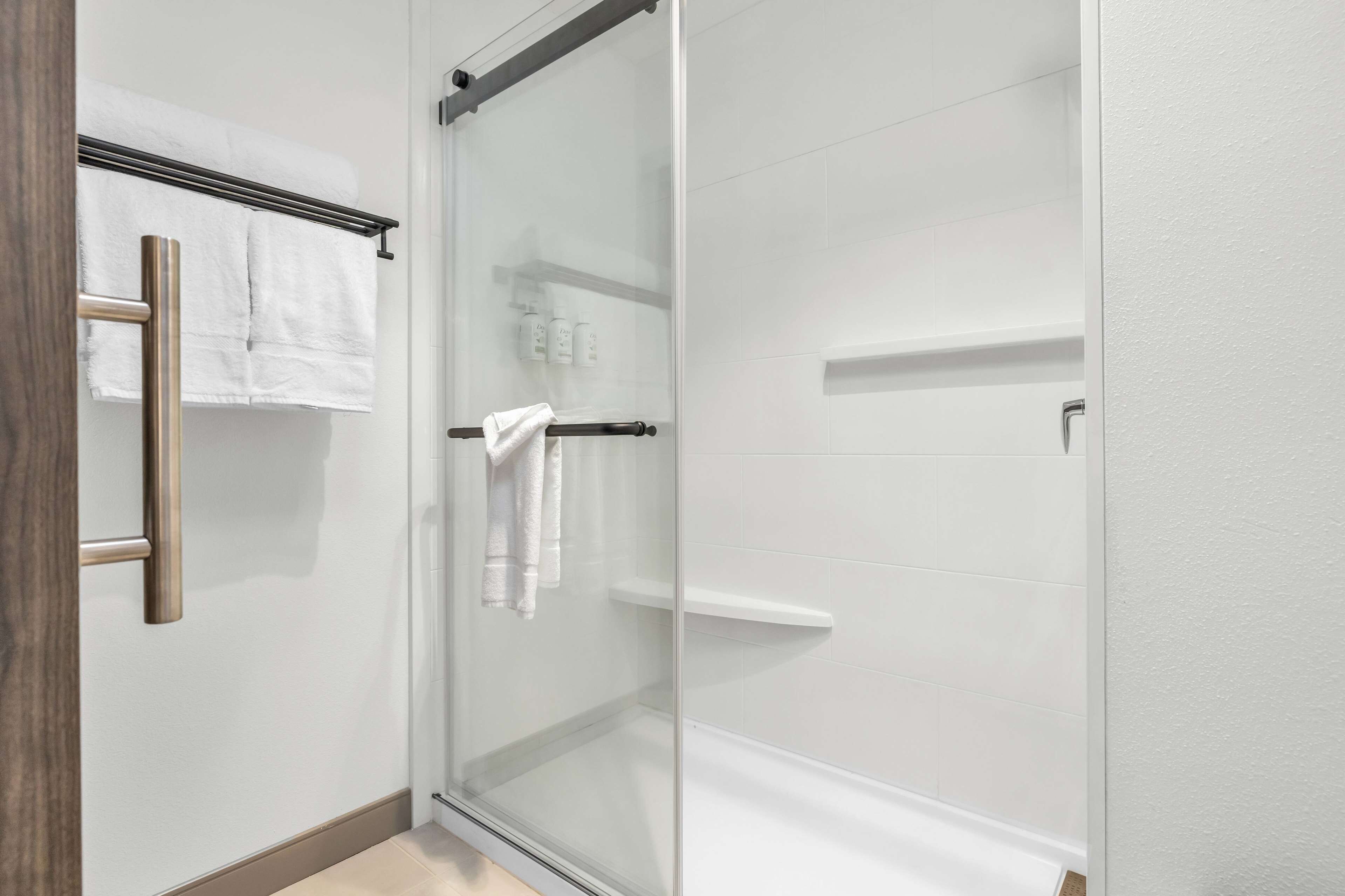 A modern bathroom with a glass shower enclosure, white tiled walls, and a wooden door.