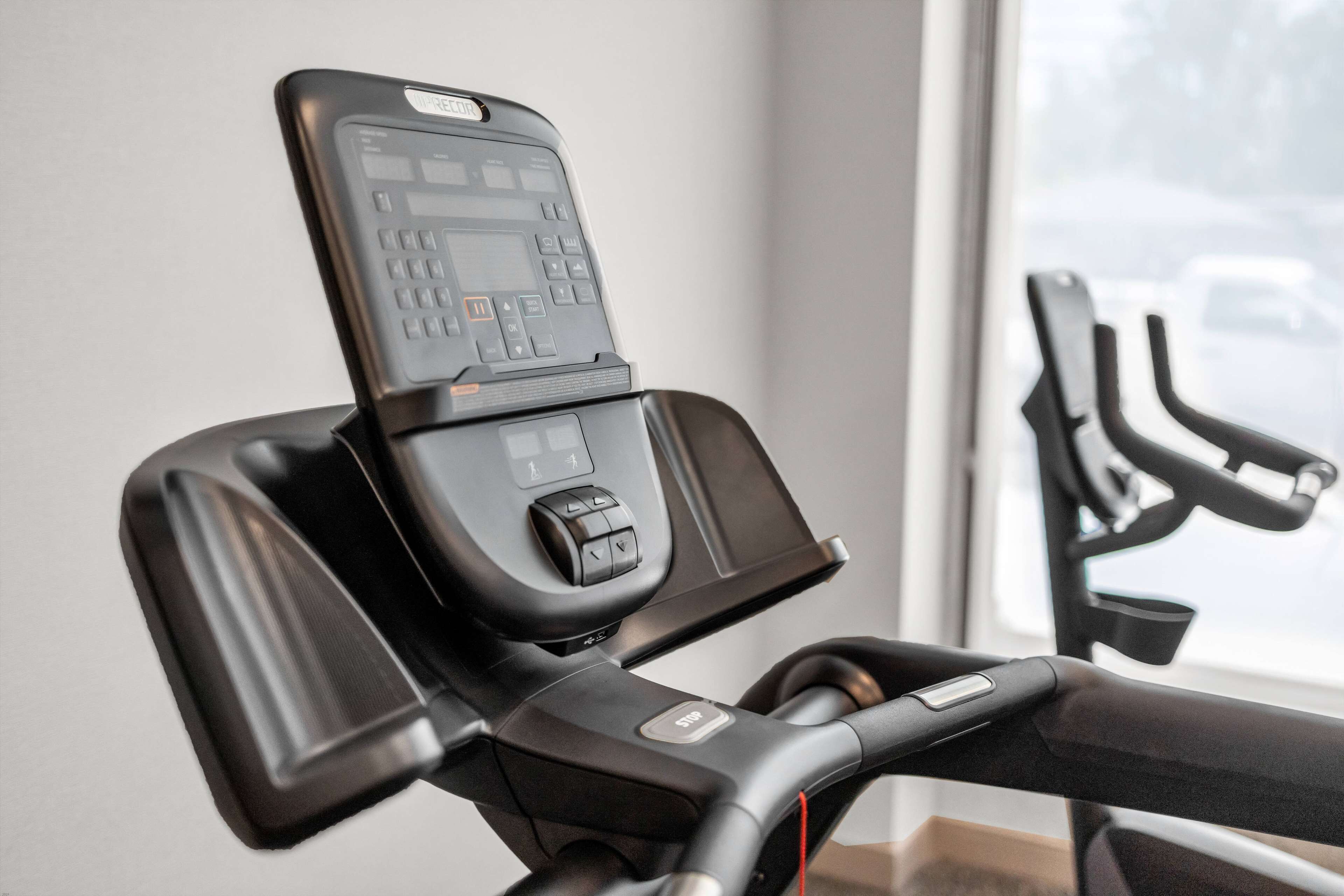 A stationary bike with a digital display and control panel, positioned near a window with a view of parked cars.