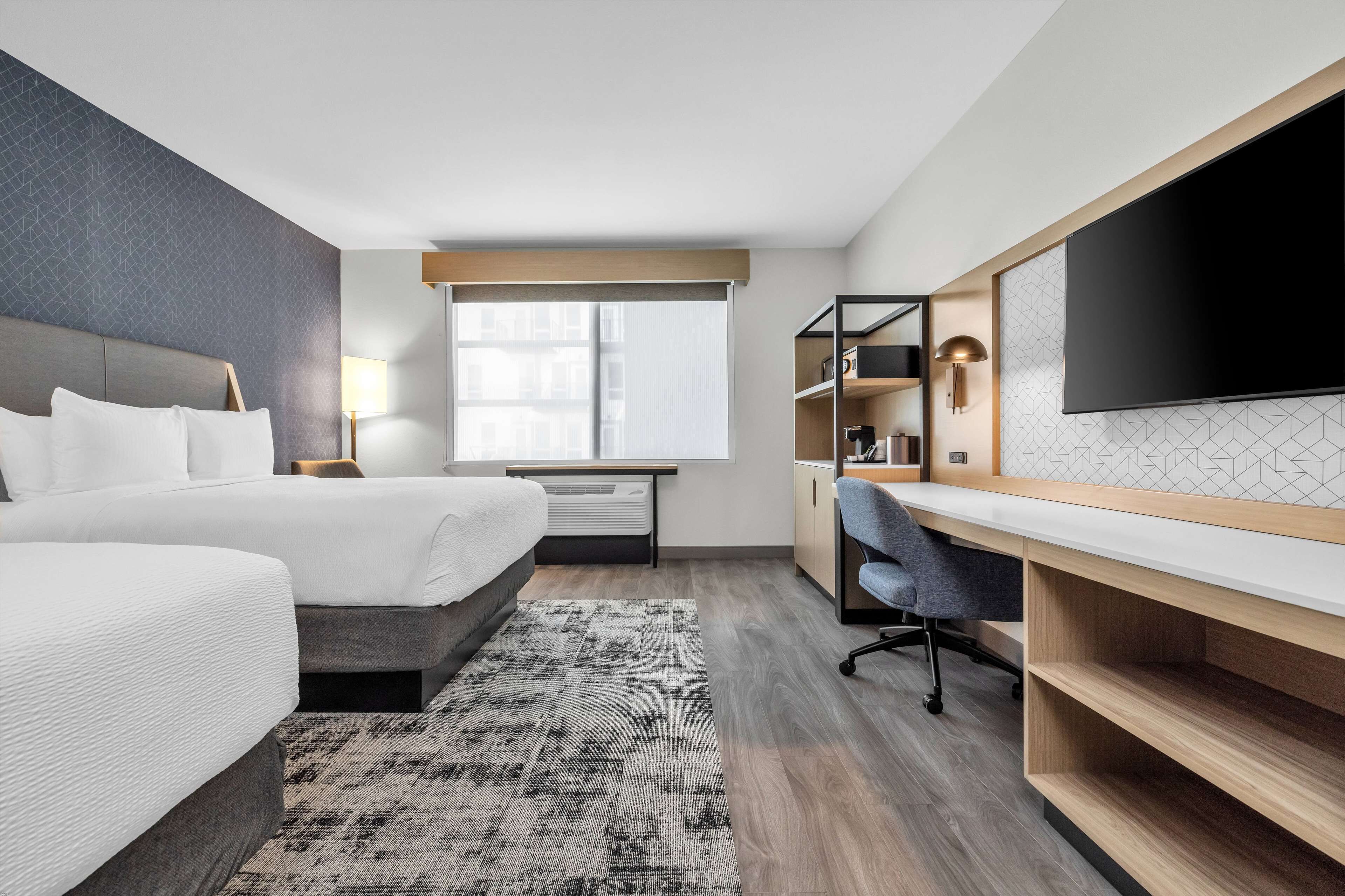 A modern hotel room with a large bed, a desk, a flat-screen TV, and a window with blinds.