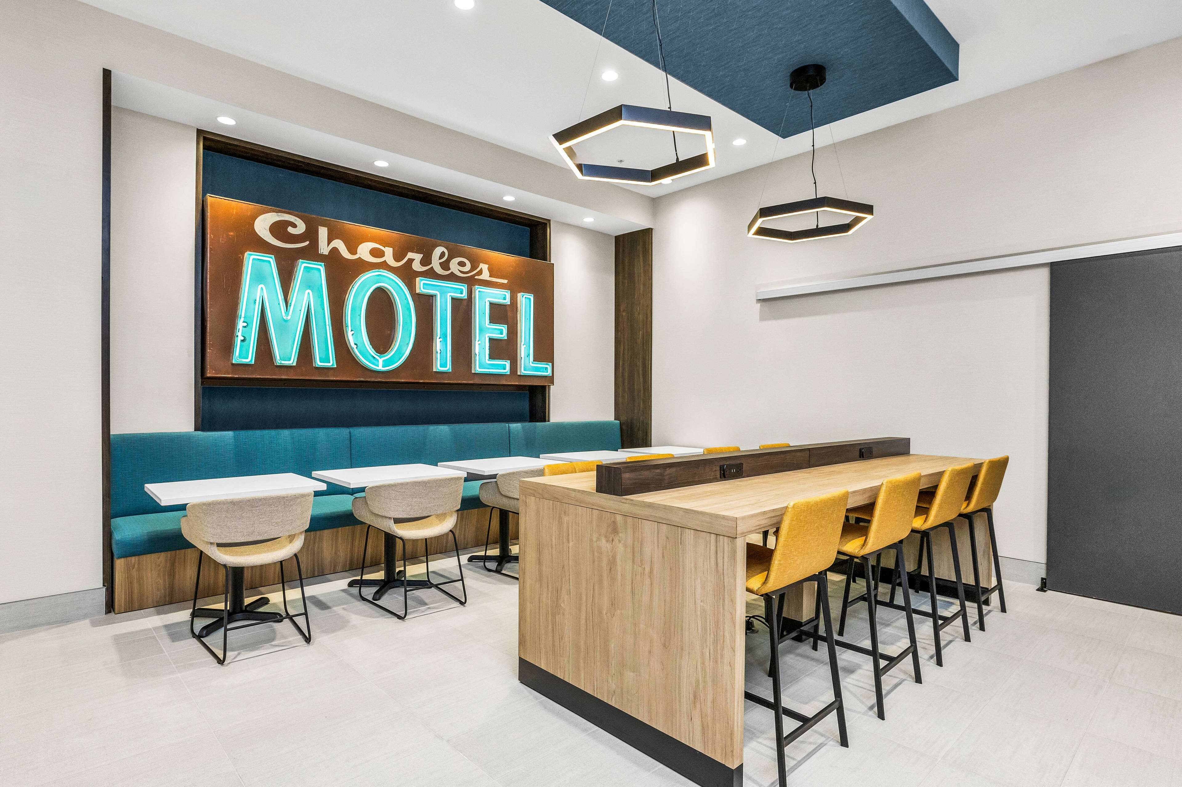 L’intérieur d’un motel moderne, avec un panneau lumineux au néon, un bar central et des espaces aménagés pour s’asseoir.