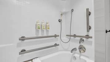 A modern bathroom with a white tiled wall, a bathtub, a shower with a handheld showerhead, and three bottles of Dove body wash.