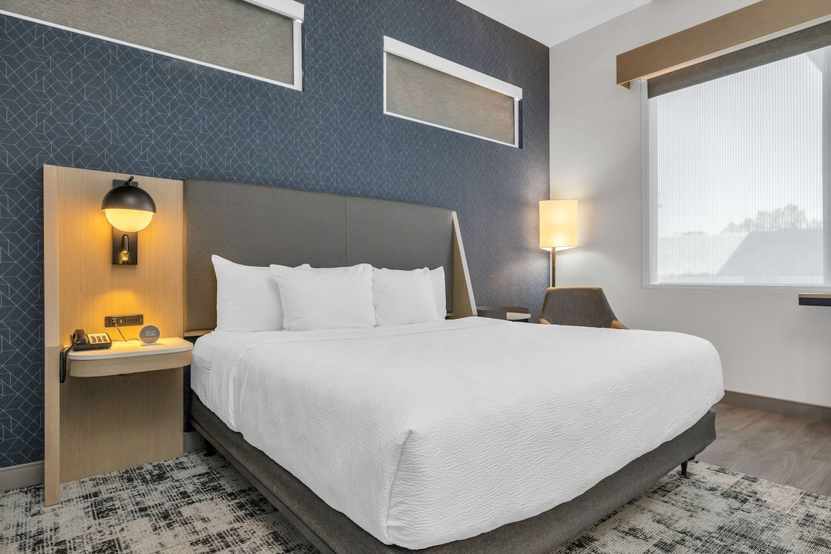 Une chambre d’hôtel avec un grand lit, des tables de chevet, une lampe fixée au mur et une fenêtre donnant sur un beau paysage.