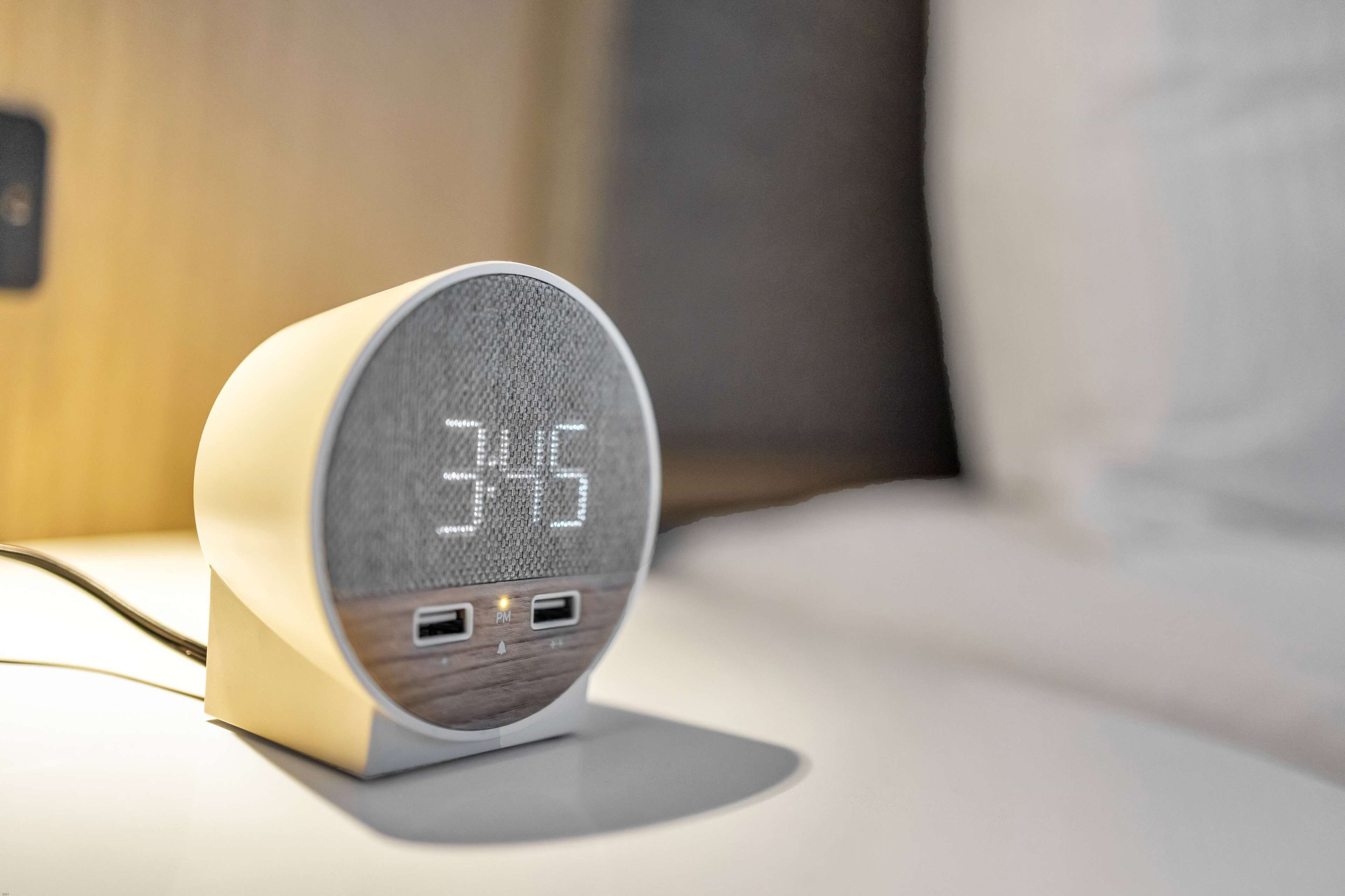 A modern alarm clock with a digital display on a bedside table.