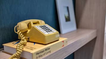 A yellow rotary phone on a wooden shelf with a book titled "A Way of Living" by Herman Miller.