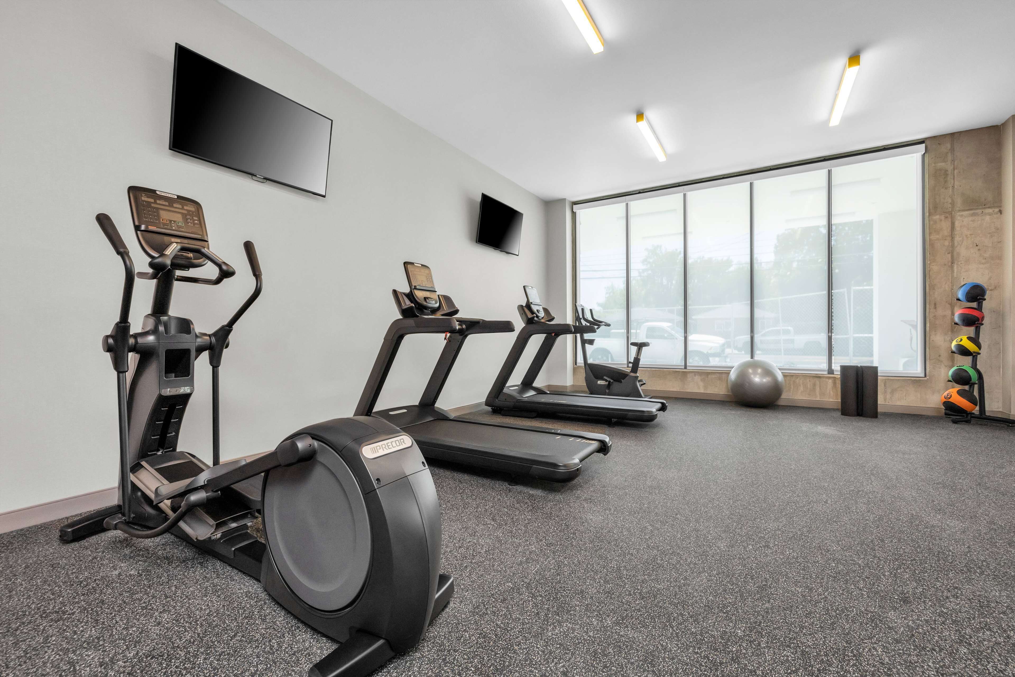 Un gimnasio con cintas de correr, elíptica, bicicleta estática y una pelota de ejercicios grande.