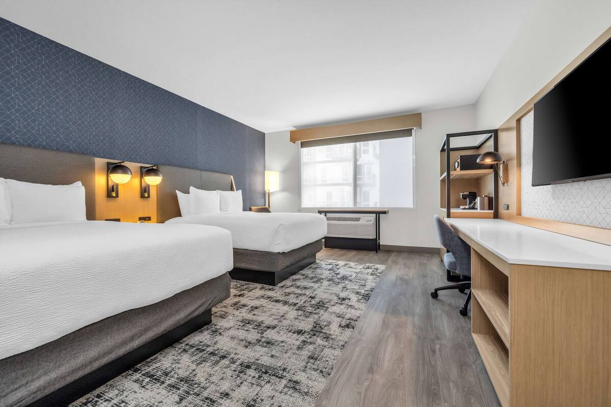 Une chambre d’hôtel avec deux lits, un bureau, une télévision et une fenêtre donnant sur un paysage agréable.